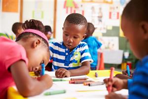 Children sitting at a table, coloring with big crayons. Children sitting at a table, coloring with big crayons.