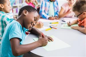 Smiling child sitting at a table with other kids, coloring with crayons.