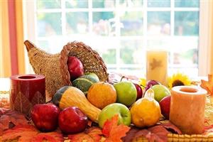 Cornucopia, candles, and fruits on a bed of fall leaves.