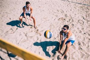 Two young men playing beach volleyball as viewed from the top of the net